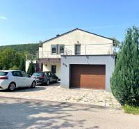 A family house in Melčice-Lieskové, with two cars parked in front, surrounded by greenery.
