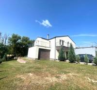A family house in Melčice-Lieskové with a parking lot and a green lawn, surrounded by trees.