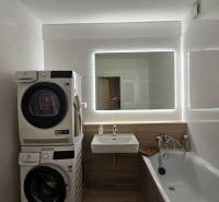 Bathroom with a bathtub, washing machine, dryer, and mirror in a 3-room apartment.