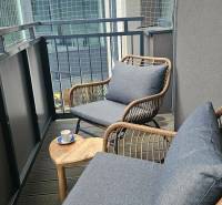 A balcony with comfortable armchairs and a table in a 3-room apartment with a wood-patterned floor.