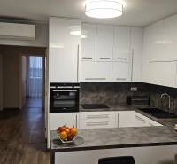 A kitchen with white cabinets, a dark countertop, and a wood-patterned floor in a 3-room apartment.