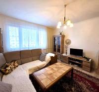 Living room of a three-room apartment with a sofa, chandelier, wood-patterned floor, and cabinets.
