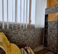 Interior of a 3-room apartment with a rattan chair, a wall with brick texture, and curtains.