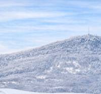 Snow-covered landscape with a dense forest and a transmitter on a hill near Banská Štiavnica.