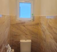A toilet with ceramic tiles and a small window in a family house.