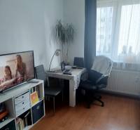 Studio apartment with a table, chairs, bookshelf, and television; floor with wood decor.