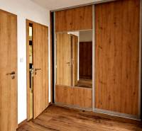 A corridor with a wooden decor floor and a mirror in a 3-room apartment.