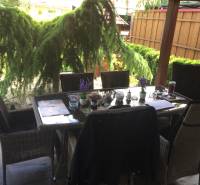 Family house with seating on the terrace, including flooring with a wooden decor and garden greenery.