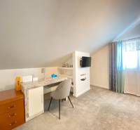 A room in a family house with a desk, a television, and a light carpet.