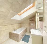A bathroom in a family house with a bathtub, a skylight, and light tiles.