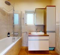 A bathroom with light tiles, a bathtub, and a sink with a wooden decor floor.