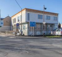 A building in Veľké Leváre, by the road, with a parked car and traffic signs.