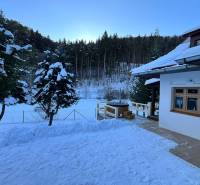 A family house in Bystrá on a snowy street with a view of the forest and snowy landscape.
