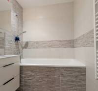 A bathroom with a bathtub and a cabinet in a 3-room apartment with white and gray tiles.
