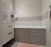 A bathroom with a bathtub, gray tiles, and a pink rug in a 3-room apartment.