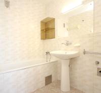 Bathroom in a 2-room apartment with light tiles and a bathtub.