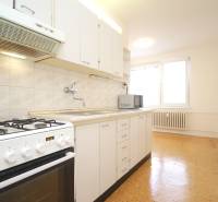 A kitchen in a 2-room apartment with white cabinets and appliances, and a floor with a wooden decor.