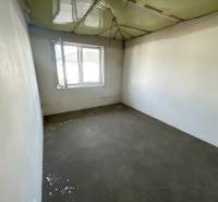 An empty room in a family house without flooring and with a green ceiling.