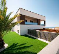 A villa in Novalja with a sea view, surrounded by a lawn and a palm tree.