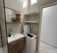 Bathroom in a 3-room apartment with a sink, washing machine, and shelves, stone-patterned floor.