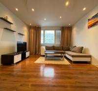 Living room with wood-patterned flooring, a sofa, and a television in a three-room apartment.