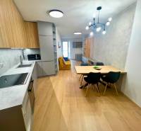 A kitchen in a 2-room apartment with a wooden decor floor, a dining table, and a modern light fixture.