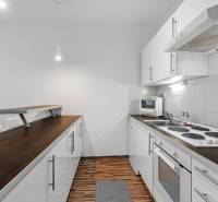 A kitchen with white cabinets, a wooden decor countertop, and appliances in a studio apartment.