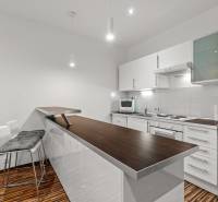 Kitchen in a studio apartment with a light-colored kitchen unit and a counter, flooring with a wooden decor.