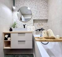 Bathroom with a bathtub, round mirror, and glass shelf in a 3-room apartment.