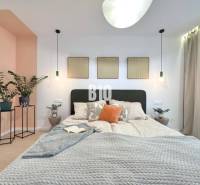 A bright bedroom with a bed, wood-patterned flooring, plants, and paintings on the wall.