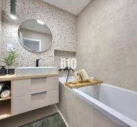 A bathroom with a sink, bathtub, round mirror, and decorative wall in a 3-room apartment.