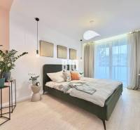 A bright bedroom with a bed and plants in a 3-room apartment with wood-patterned flooring.