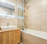 Bathroom in a 2-room apartment with a bathtub and a sink on a wooden cabinet.