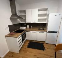 The kitchen in the 2-room apartment on Brečtanová Street with wooden flooring and white furniture.