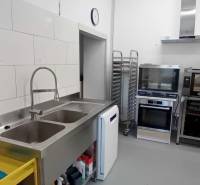 Kitchen equipment with appliances and sink in warehouse and hall spaces.