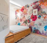 A bedroom in a 4-room apartment with colorful floral wallpaper, a bed, and a wooden storage cabinet.