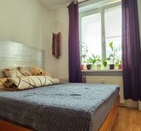 A bedroom in a 2-room apartment with light streaming through the window and a floor with a wood decor.