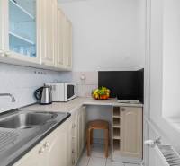 A kitchen in a studio apartment with appliances, fruit, and cabinets, with a marble countertop.