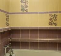 A bathroom with colorful tiles and a bathtub, decorative flowers, and a shelf in a two-room apartment.