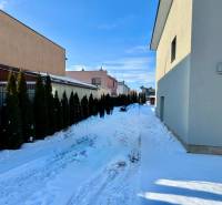 Snow-covered Gyňovská Street in Čaňa with family houses and a hedge.