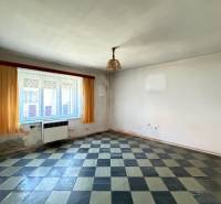 A room in a family house with a checkered floor, window heating, and orange curtains.