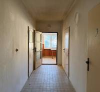 A hallway in a family house with tiles leads to a well-lit room.