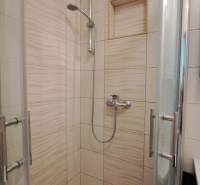 A shower corner in a 2-room apartment with cream-colored tiles and glass doors.