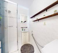 A bathroom in a 3-room apartment with a sink, shower, and shelves.