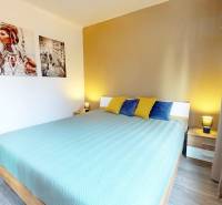 A bedroom with a bed, colorful pillows, a nightstand, and a wooden decor floor in a 3-room apartment.