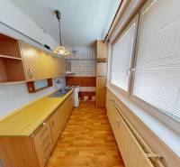 A kitchen in a three-room apartment with a wooden decor floor and light cabinets.