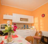 A kitchen in a family house with orange walls, white cabinets, and flowers on the table.