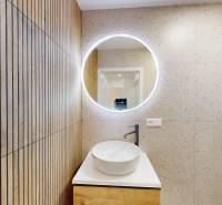 A hallway from a 4-room apartment with a sink, a mirror, and a wall with a wooden decor.