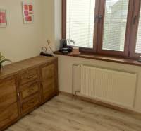 Office with a chest of drawers, flowers, and a wooden-patterned floor.