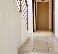 A hallway in the offices with tiles, stairs, and wooden railing leads to the door.